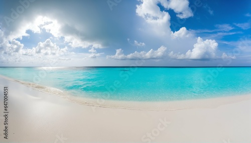 Sandy beach featuring white sand and rolling calm wave of turquoise ocean on sunny day, white clouds in blue sky background