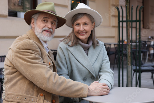 Portrait of affectionate senior couple sitting in outdoor cafe, space for text