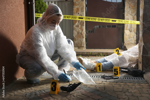 Criminologist in protective gloves working at crime scene with dead body outdoors photo