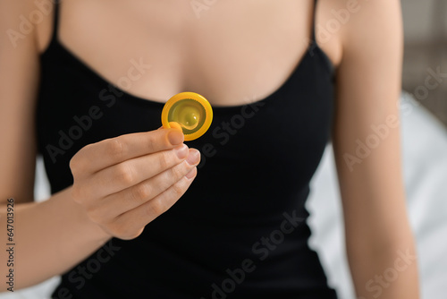 Woman holding unpacked condom on blurred background, closeup. Safe sex