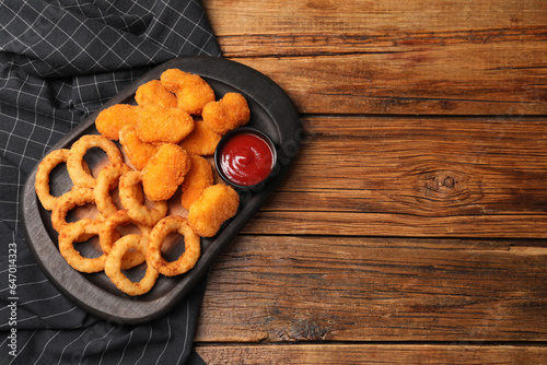 Tasty ketchup, onion rings and chicken nuggets on wooden table, top view. Space for text