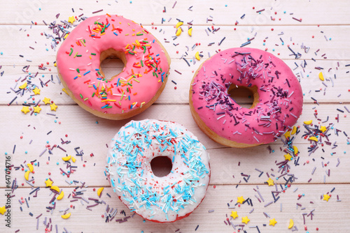 Glazed donuts decorated with sprinkles on white wooden table, flat lay. Tasty confectionery