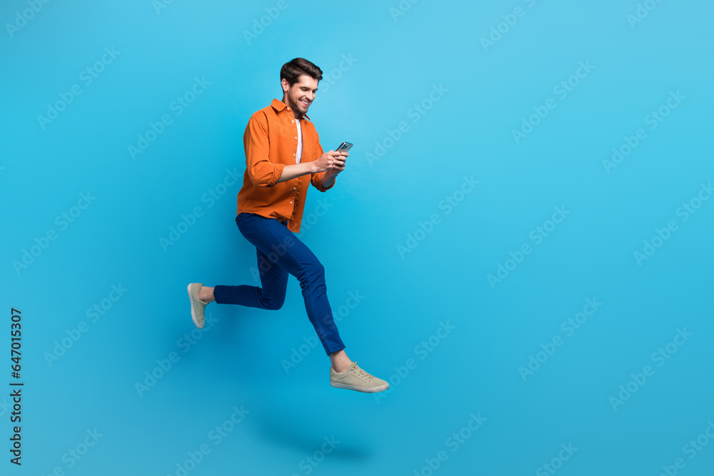 Full size profile photo of energetic attractive man use smart phone jumping run hurry empty space ad isolated on blue color background