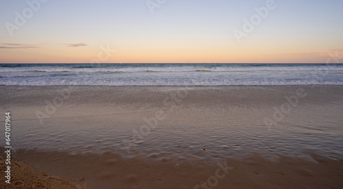 Looking east over the Pacific Ocean, Queensland, as the sun sets in the west, waiting for the full moon to rise above the horizon while the surf waves break on a sandy beach at Kawana, Sunshine Coast.