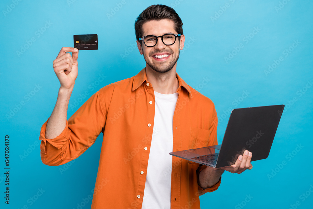Photo of cheerful handsome guy toothy smile hold showing debit plastic card use netbook isolated on blue color background Photo of cheerful handsome guy toothy smile hold showing debit plastic card use netbook isolated on blue color background