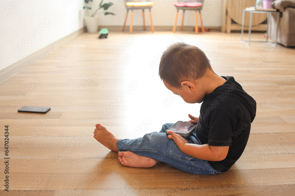 Cute Asian little kid enjoying playing with mobile phone at home