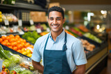 Smiling young Hispanic male supermarket worker looking at the camera, with fresh produce in the background