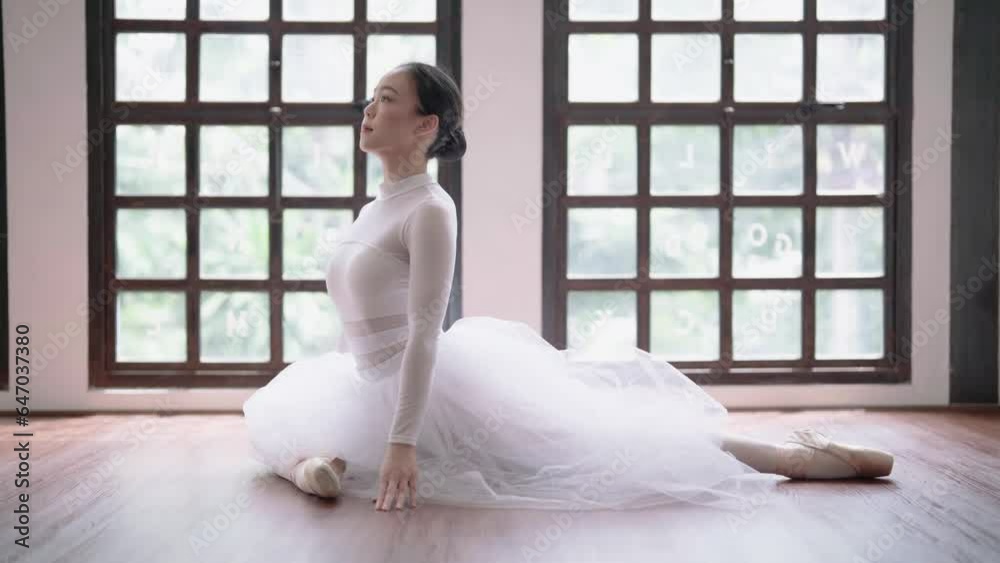Young Asian ballet dancer in white tutu practicing ballet exercises bending forwards over her stretched body while sitting on the floor. Young Asian ballet dancer in white tutu practicing ballet exercises bending forwards over her stretched body while sitting on the floor.