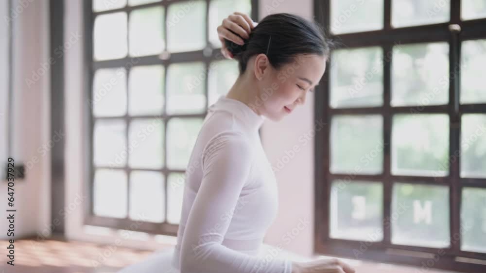 Asian Female ballet dancer sitting on the floor and wearing ballet shoes slippers as she prepares for a rehearsal in dance studio. Asian Female ballet dancer sitting on the floor and wearing ballet shoes slippers as she prepares for a rehearsal in dance studio.