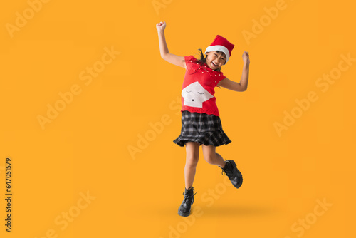 Happy smiling Asian child girl with wearing a red Christmas costume and Santa Claus hat, Celebration dancing and jumping have fun full body portrait, isolated on yellow background