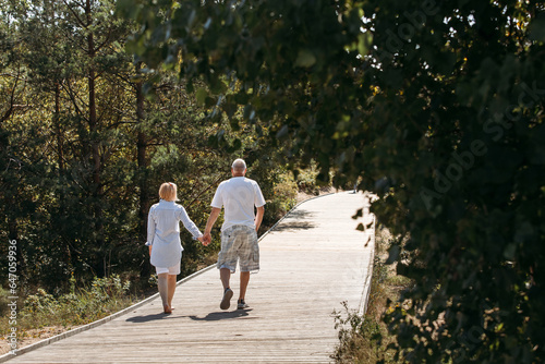 Happy elderly couple walking on a wooden deck on a forest path in the sand dunes