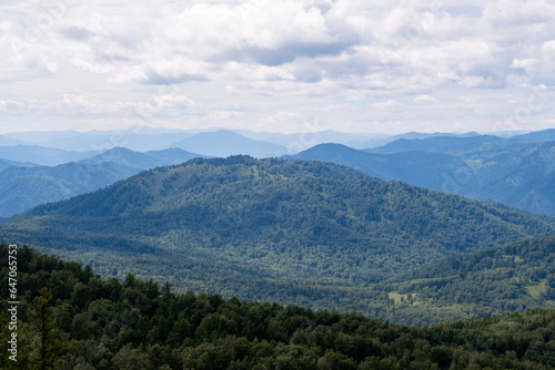 Amazing view of mountains and forest landscape with cloudy skies Altai mountains. Natural green landscapes against the background of clouds, and below the village of Manzherok, Altai Republic, Russia.