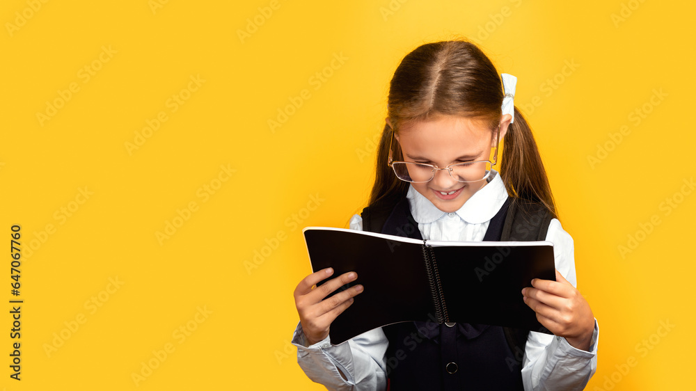 Fototapeta premium Cheerful Schoolgirl Reading notebook Learning Over Yellow Background In Studio. School Education Concept