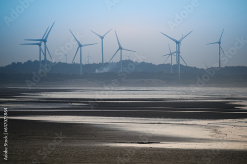 Fans of wind turbines spin over the sparkling sea. Dynamic clouds at sunset. An offshore wind farm off the northwest coast of Taiwan. One of green power.