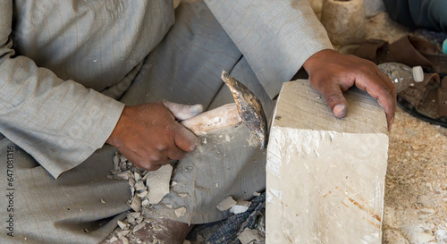 A man traditionally creating Egyptian sculptures by hand with stone chips flying off