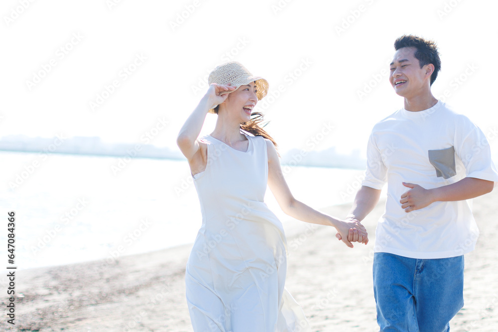 手を握ってビーチを歩いている若いアジア人のカップル