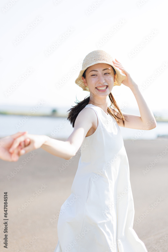 夏の若いアジアの女性は、ビーチで恋人の手を握る服を着ています