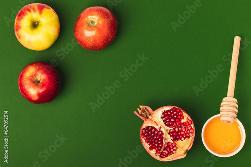 Honey, three apples and half a pomegranate on a green background. Rosh Hashanah holiday. Jewish New Year. Flat composition. photo