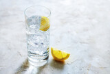 Fresh carbonated mineral water with ice cubes and lemon slices in a drinking glass, refreshing drink on a light stone background, copy space, selected focus