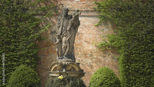 A sandstone statue of a saint with a cross and a golden halo in the Brevnov Monastery garden in Prague. photo