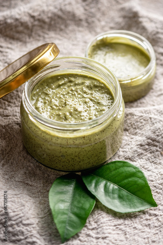 Natural green scrub with sugar in a glass jar on the background of cloth and leaves. Concept of organic cosmetics and skin care