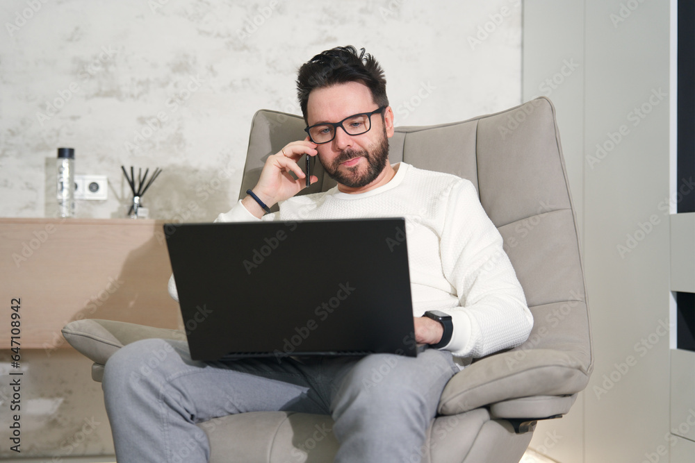 Young happy successful man in glasses working on laptop computer at home and talk on cell mobile phone Young happy successful man in glasses working on laptop computer at home and talk on cell mobile phone