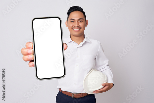Professional engineer young Asian men wearing formal shirts and protective construction helmet holding big smartphone with blank screen while smiling expressions isolated on white background