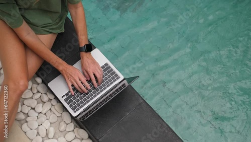 Female freelancer working with laptop in the swimming pool at sunny day. High quality 4k footage
