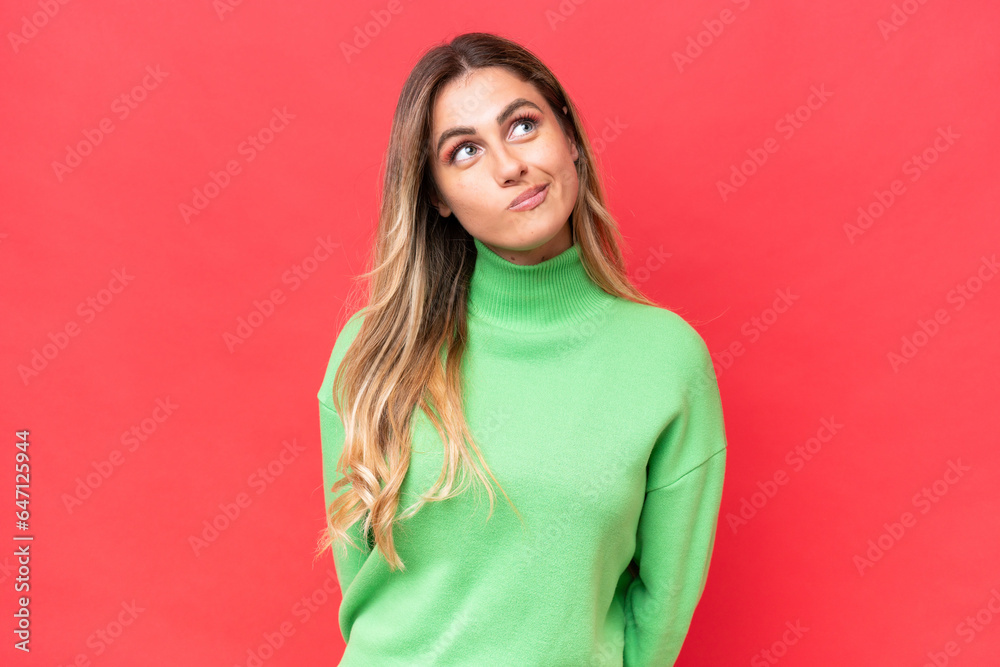 Fototapeta premium Young Uruguayan woman isolated on red background and looking up