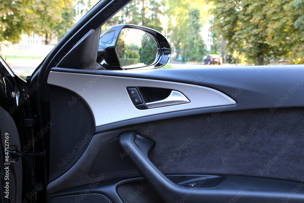 Elegant design of luxury car door trim. Door trim elements and door handle with rear view mirror. View from inside the car. Side rear-view mirror on a modern car. Luxury car door interior trim