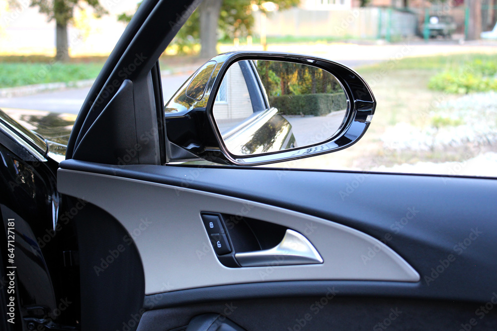 Rear view mirror with door trim elements and door handle. View from inside the car. Side rear-view mirror on a modern car. Close up rearview mirror lux car.