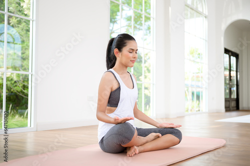 Young woman in sportswear doing meditation practice and yoga indoor, healthy lifestyle, Mental health concept.
