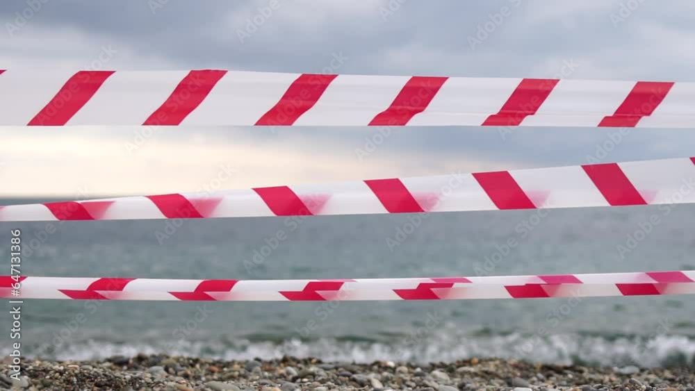 Red white warning tape barrier ribbon swinging in the wind across exotic sea beach background without people. No entry Red White caution tape. No holiday concept, delayed travel, no summer plans Red white warning tape barrier ribbon swinging in the wind across exotic sea beach background without people. No entry Red White caution tape. No holiday concept, delayed travel, no summer plans