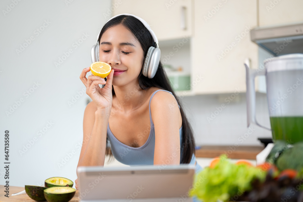 A relaxed Asian woman is smelling a lemon and enjoying making her healthy meal in the kitchen. A relaxed Asian woman is smelling a lemon and enjoying making her healthy meal in the kitchen.