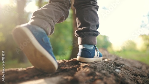 baby boy playing in the forest park. close-up child feet walking on a fallen tree log. happy family kid dream concept. a child in sneakers walks on a fallen tree in park lifestyle