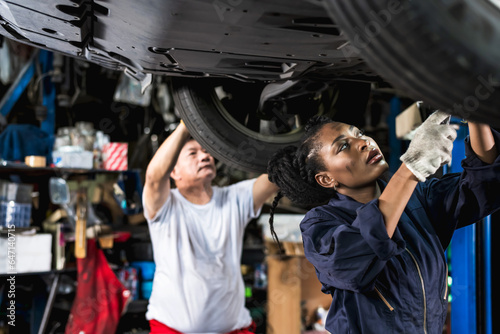 Black auto mechanic woman working in auto repair shop with Asian technician man background