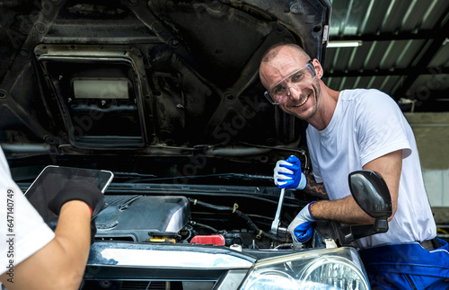 Smiling auto mechanic with wrench changing car engine in repair shop