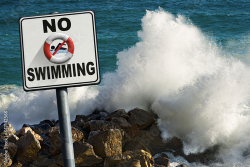 No swimming sign. Large waves of the sea break on the rocks on background.