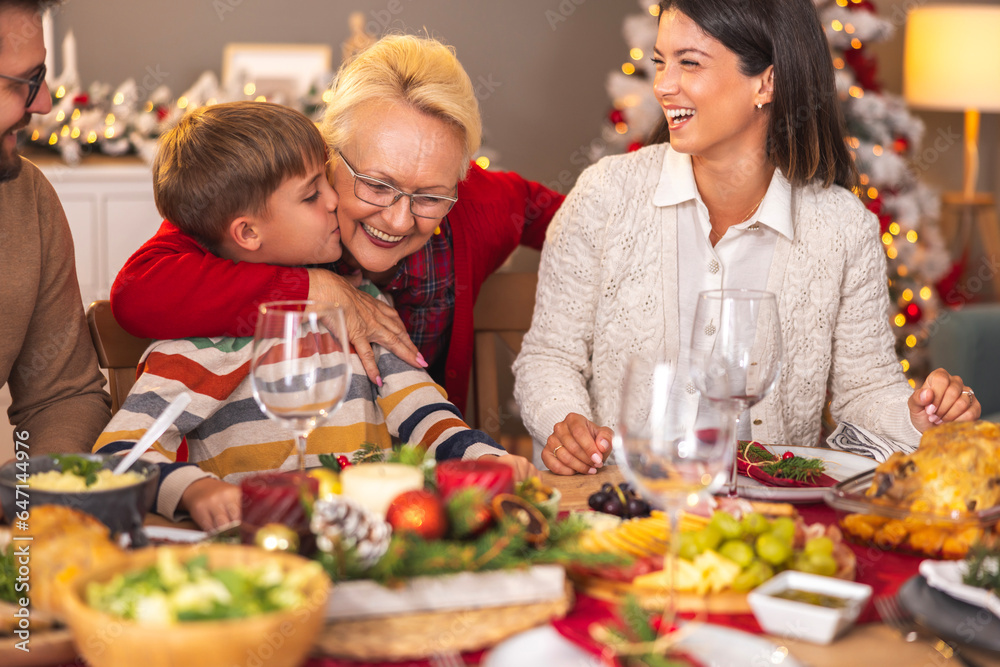 Little boy kissing his grandmother while having family Christmas dinner at home