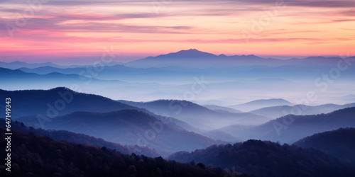 The mountains are shrouded in mist, and the last traces of daylight lend a tranquil, mystical quality to the scene. A twilight shot of autumn mountains under a fading pink and purple sky. © tashechka