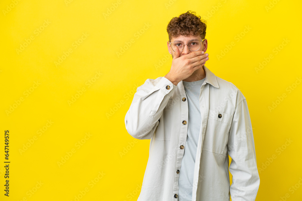 Young handsome caucasian man isolated on yellow background covering mouth with hand Young handsome caucasian man isolated on yellow background covering mouth with hand