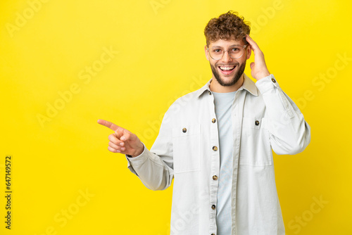 Young handsome caucasian man isolated on yellow background surprised and pointing finger to the side