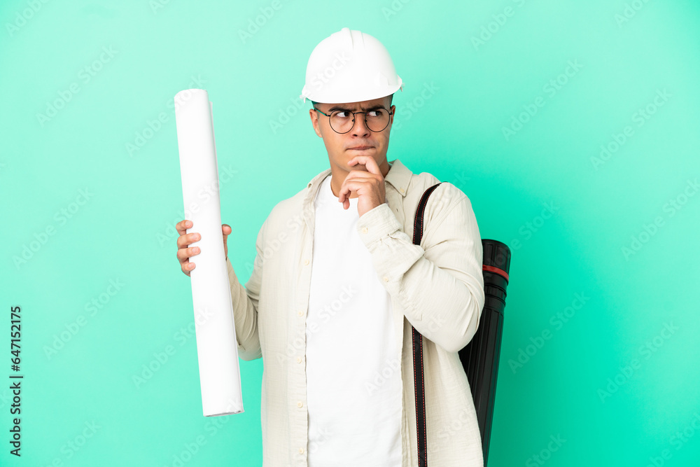 Young architect man holding blueprints over isolated background having doubts and thinking Young architect man holding blueprints over isolated background having doubts and thinking