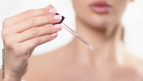 Close-up studio portrait of a young woman, isolated on a light background, applying serum from a pipette. Natural organic cosmetic product for facial skin care and skin regeneration.