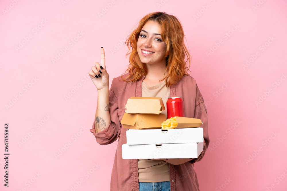 Young caucasian woman holding fast food isolated on pink background showing and lifting a finger in sign of the best Young caucasian woman holding fast food isolated on pink background showing and lifting a finger in sign of the best