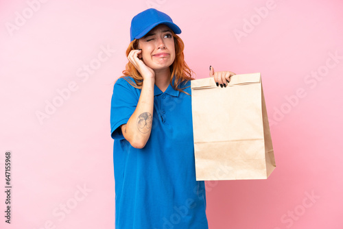 Young caucasian woman taking a bag of takeaway food isolated on pink background frustrated and covering ears