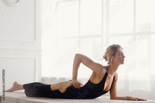 Athletic woman in black sporty uniform practicing yoga in light studio, The woman's impressive pose serves as an inspiration for others to push their limits
