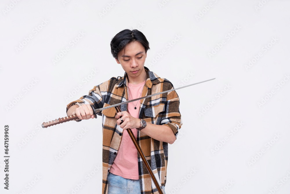 A young asian man puts back a ceremonial katana into its sheath. A sword enthusiast feeling like a samurai warrior. Isolated on a white background.
