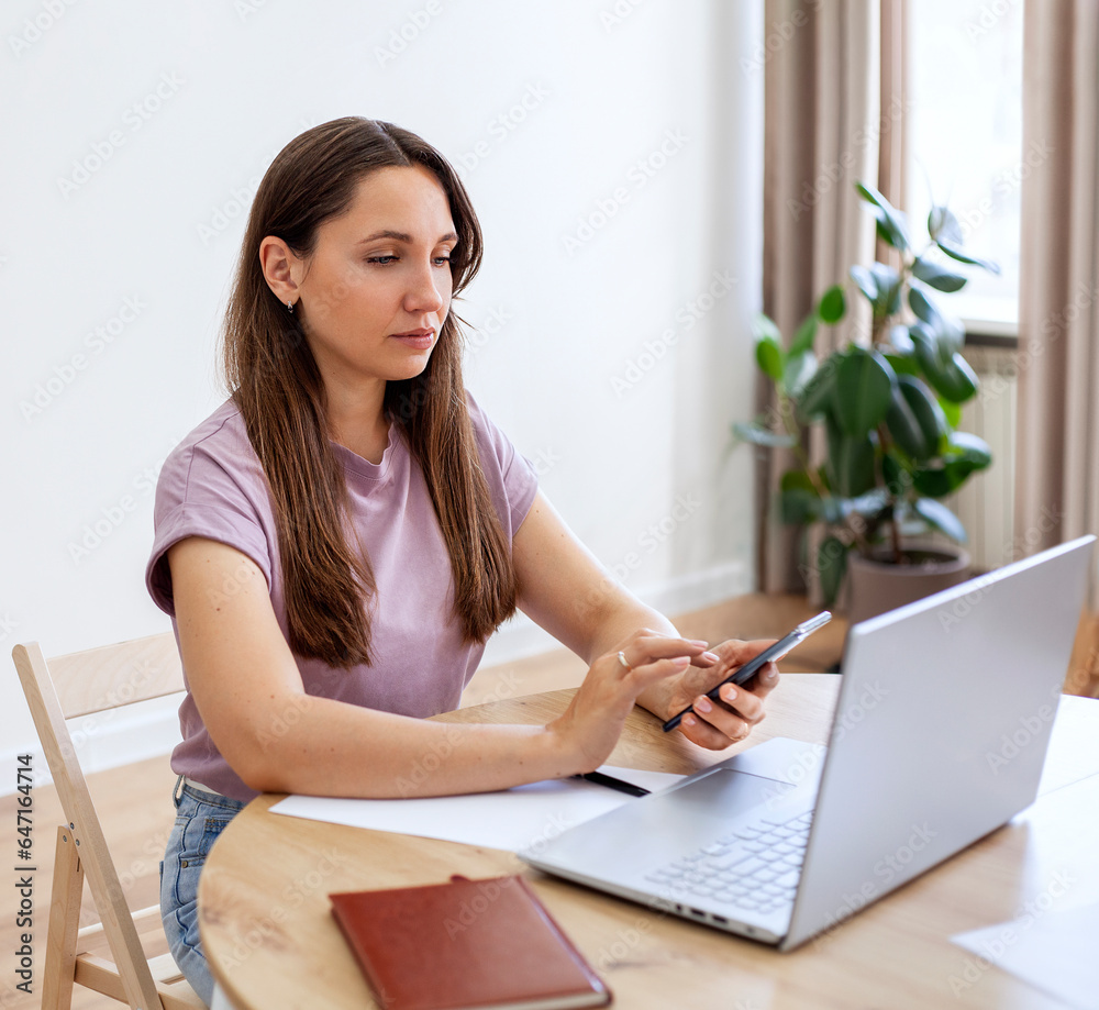 Obraz premium Portrait of a young woman using mobile phone and laptop at home