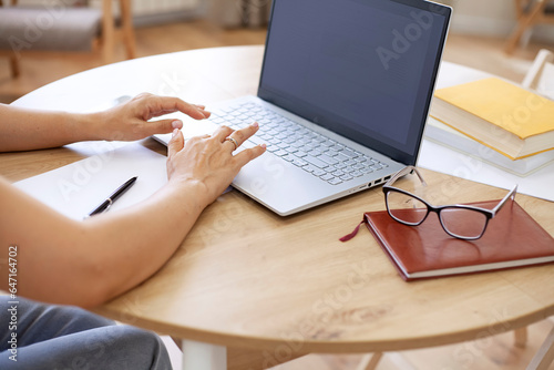 Woman working on laptop at home, close-up of hands.